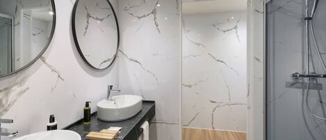 A modern bathroom with a large white sink, a round mirror, and a glass-enclosed shower.