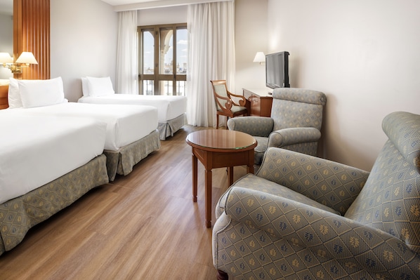 Une chambre d’hôtel avec deux lits, un canapé, un fauteuil, une petite table et un téléviseur.