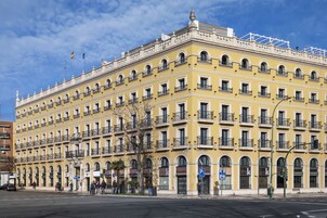 A multi-story yellow building with balconies, arched windows, and a prominent entrance.