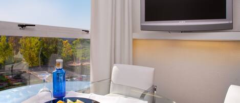 Habitación de hotel con una mesa de comedor preparada para dos personas, un televisor de pantalla plana en la pared y vista a un paisaje verde por la ventana.