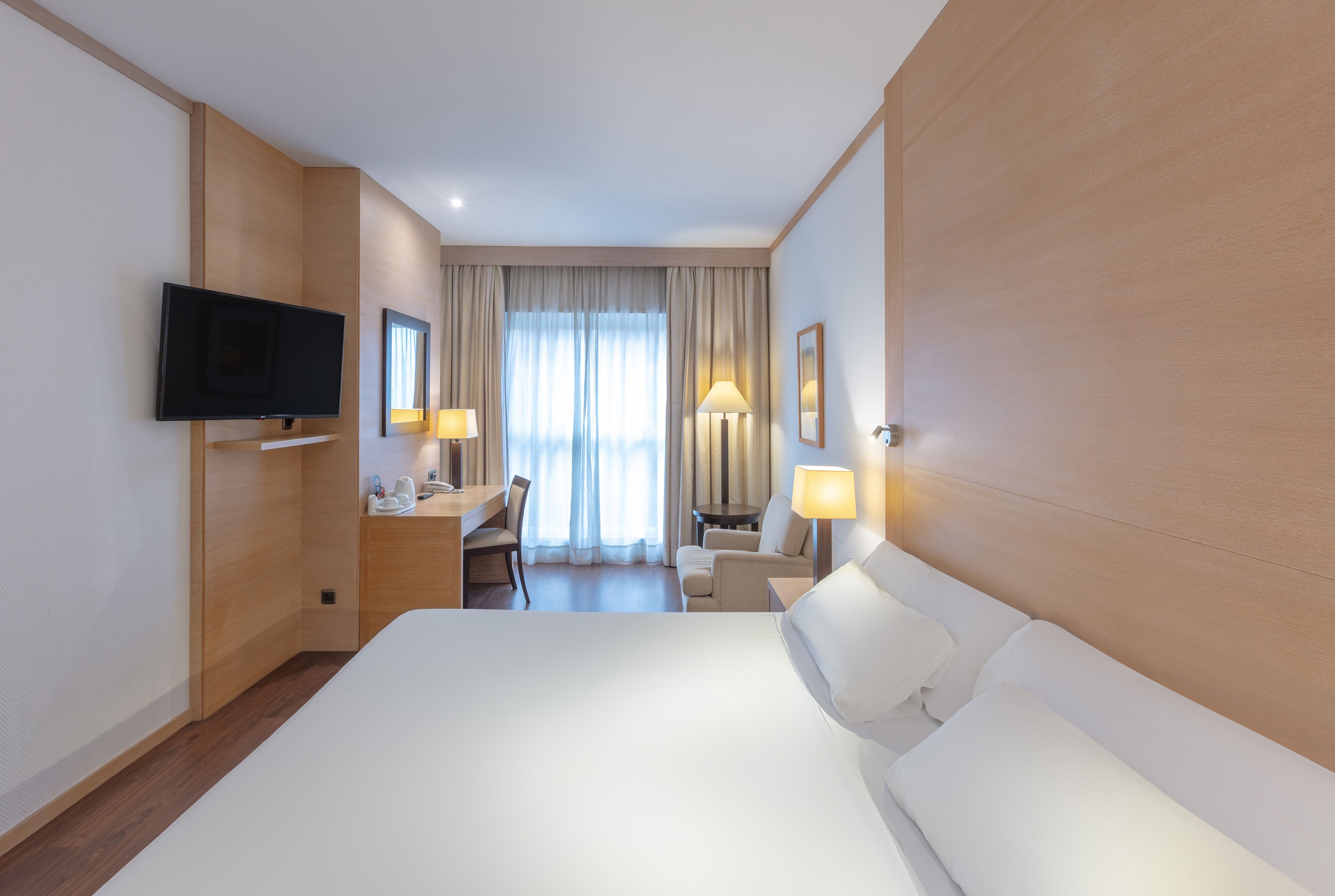 Une chambre d’hôtel avec un grand lit, un bureau avec une chaise, une télévision et deux lampes.