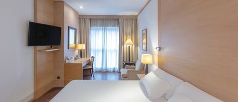 A hotel room with a large bed, a desk with a chair, a television, and two lamps.