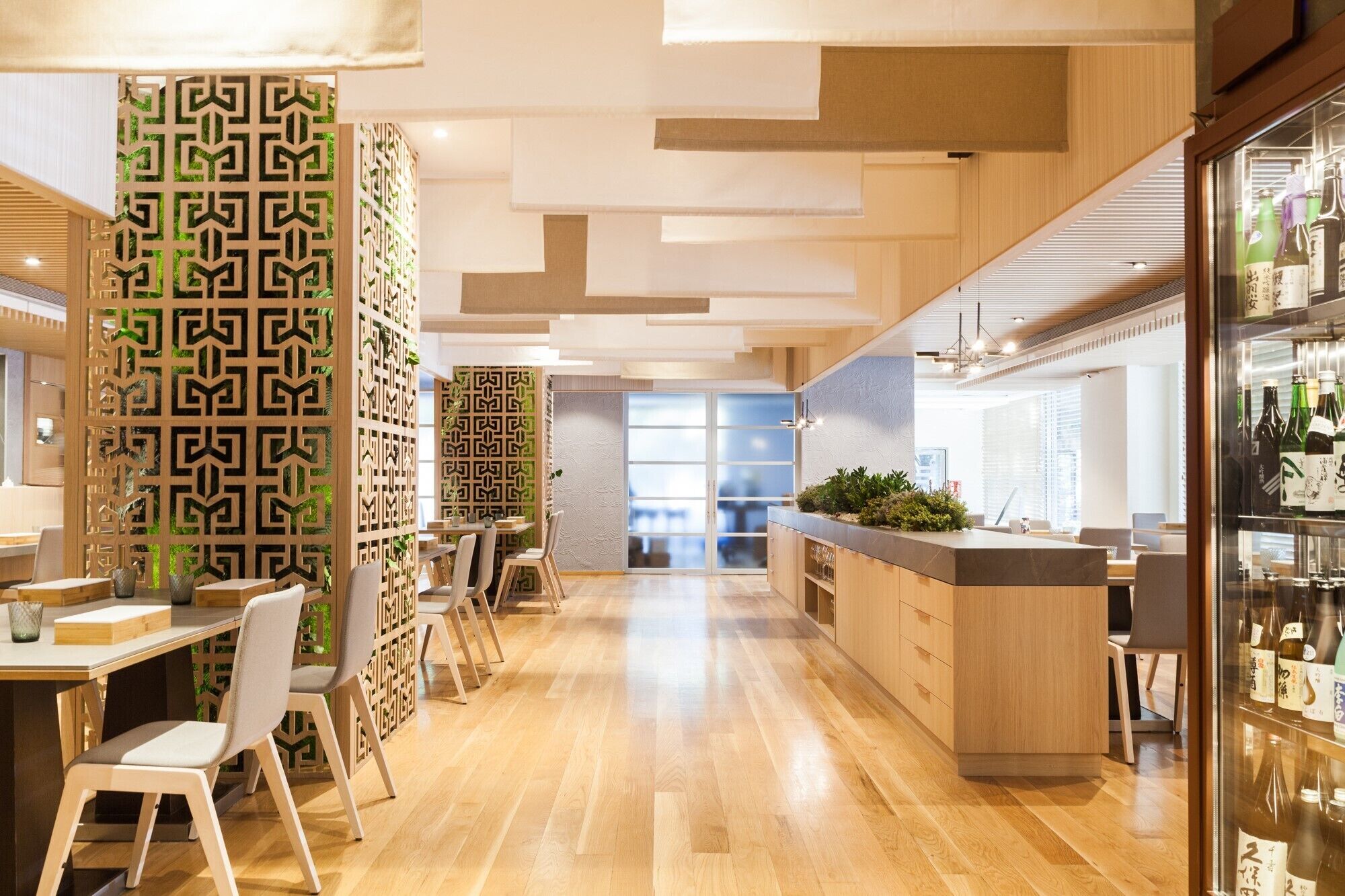Un interior moderno con suelo de madera, una isla central con una planta y una vitrina de vidrio con botellas.