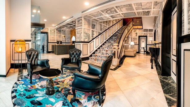 Un hall d’entrée avec un escalier, des fauteuils en cuir noir, un tapis à motifs et un comptoir d’accueil.