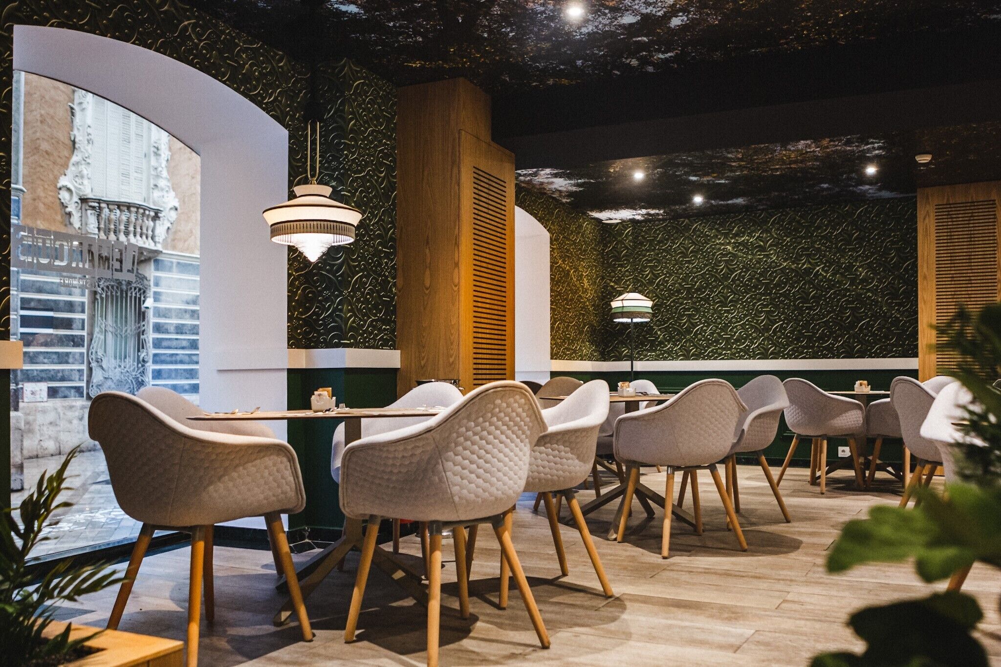 Een restaurant met een modern interieur, met een gebogen muur met een muurschildering, houten details en gestoffeerde stoelen.