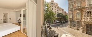 A modern bedroom with a large bed, a glass door leading to a balcony, and a view of a historic building with ornate architecture. - SH Ingles Boutique Hotel (Valencia)