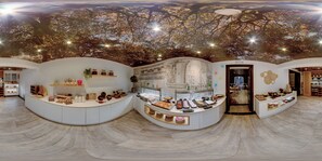 A modern interior with a curved counter displaying various food items and a ceiling mural of a tree. - SH Ingles Boutique Hotel (Valencia)