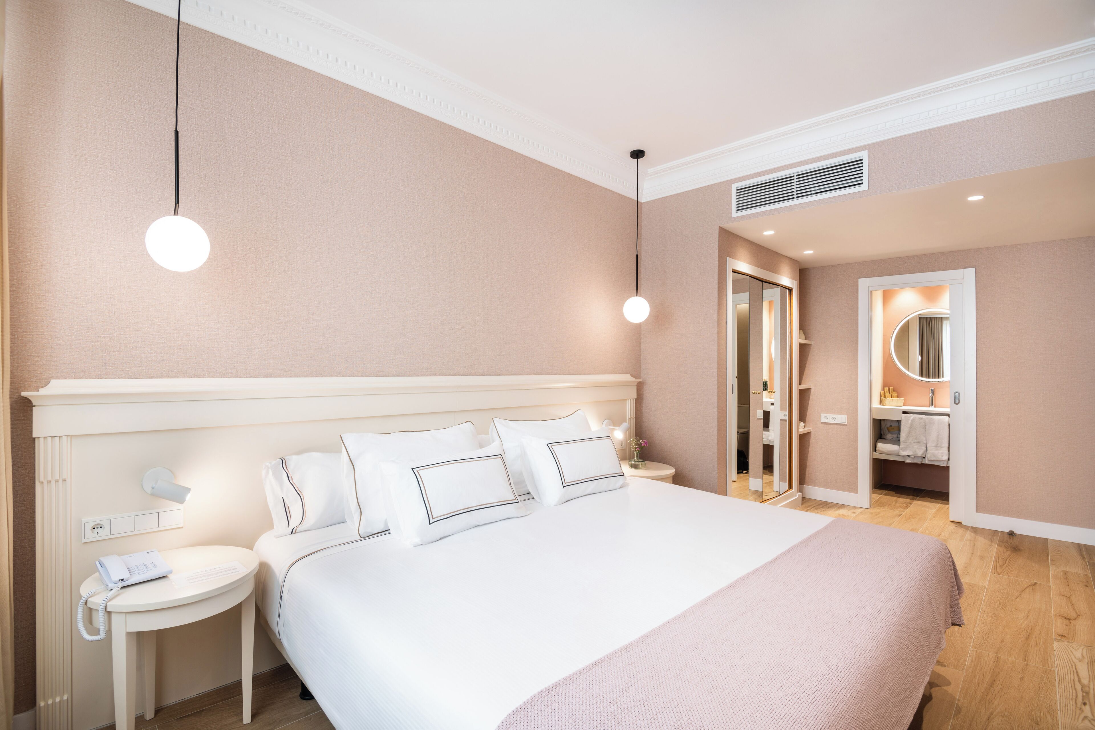 Habitación de hotel con una cama grande, mesitas de noche, un espejo y un baño visible a través de una puerta abierta.
