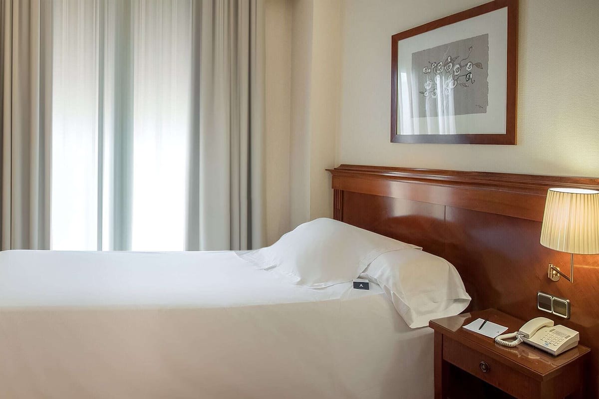 A hotel room with a bed, a desk with a chair, a telephone, and a framed picture on the wall.