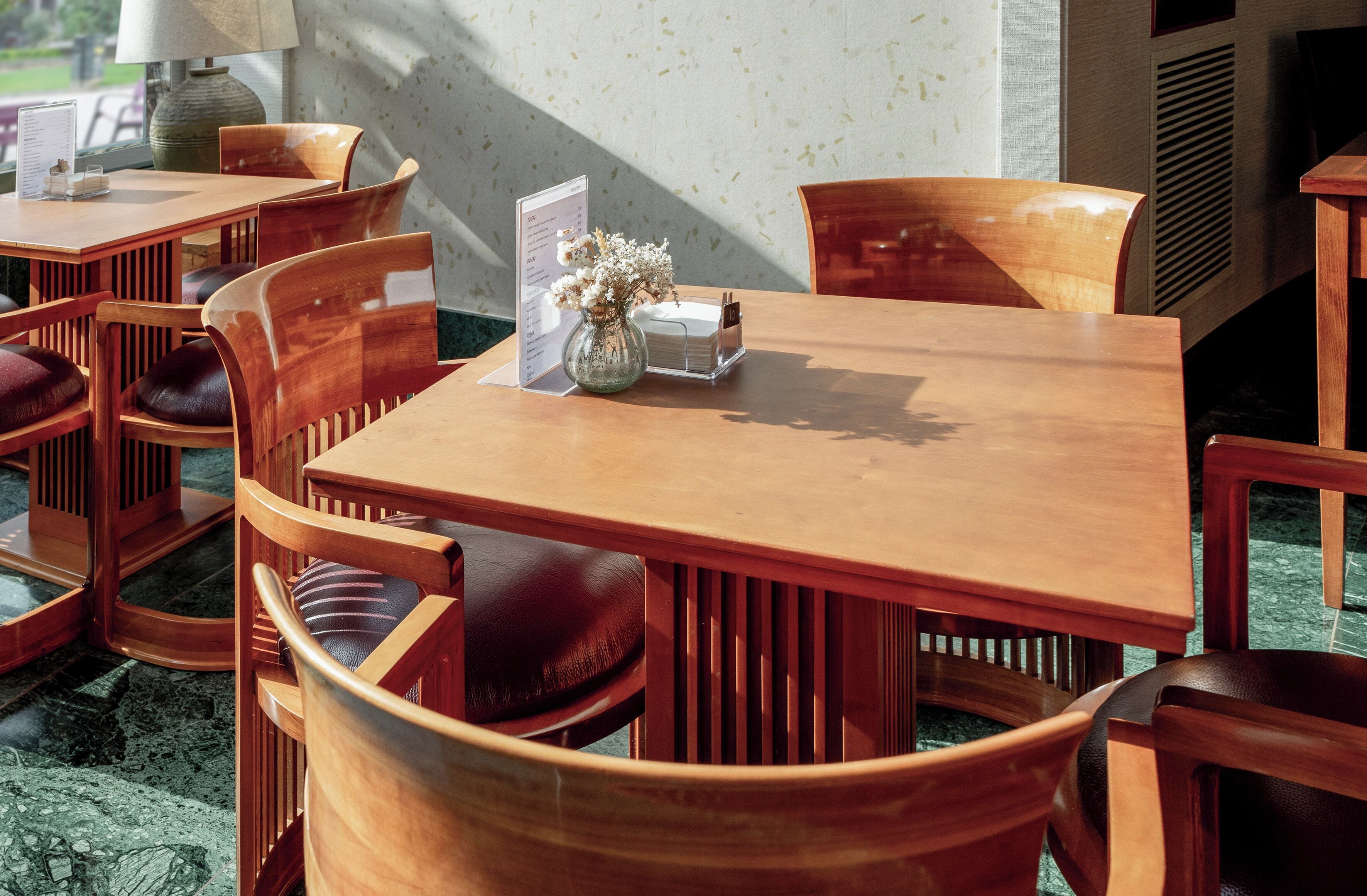Una mesa de comedor de madera con un atril para el menú, un jarrón con flores y varias sillas de madera con asientos acolchados.