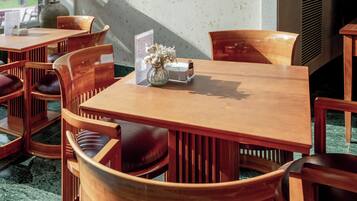Una mesa de comedor de madera con un atril para el menú, un jarrón con flores y varias sillas de madera con asientos acolchados.