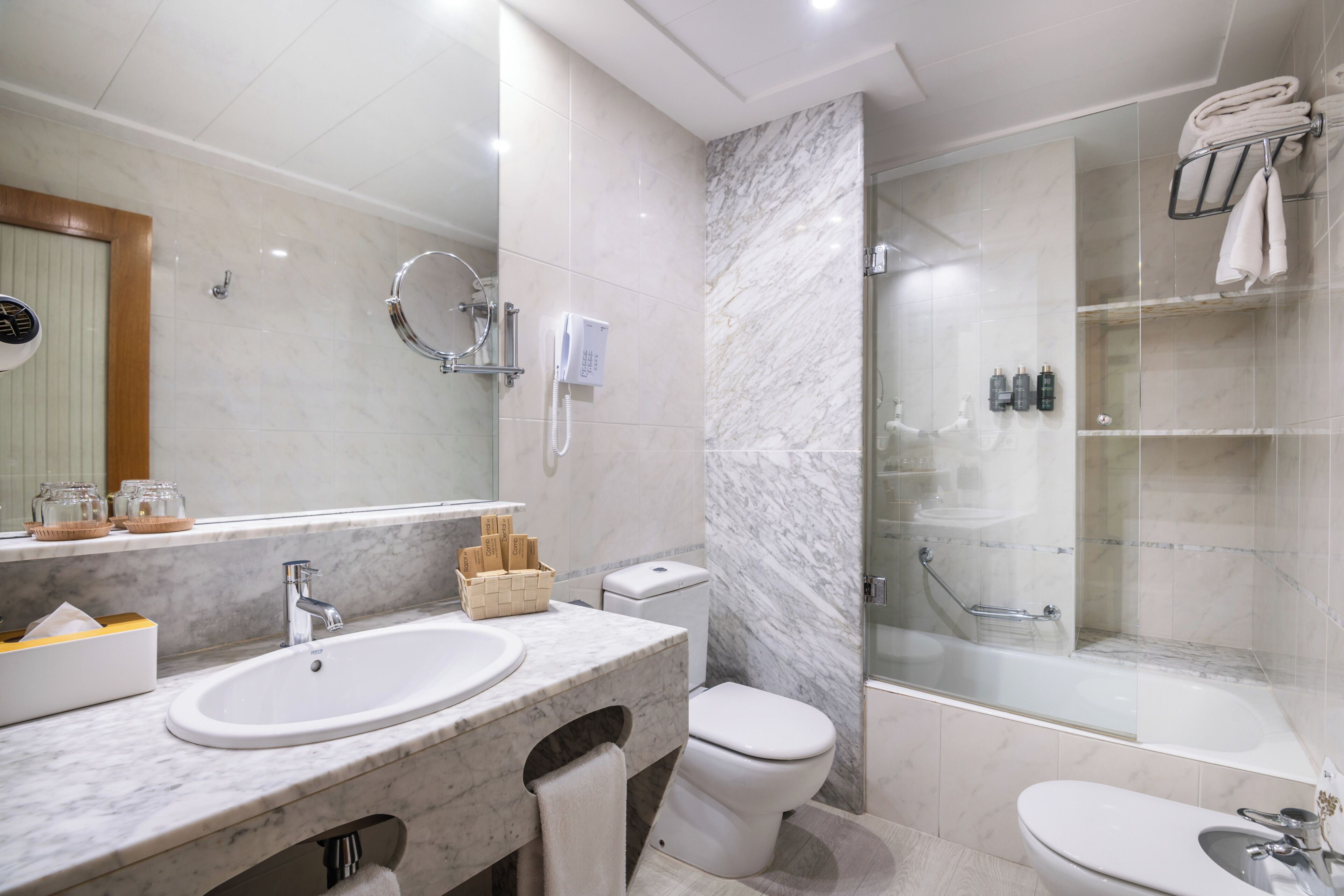 A modern bathroom with a marble sink, toilet, and a glass-enclosed shower area.