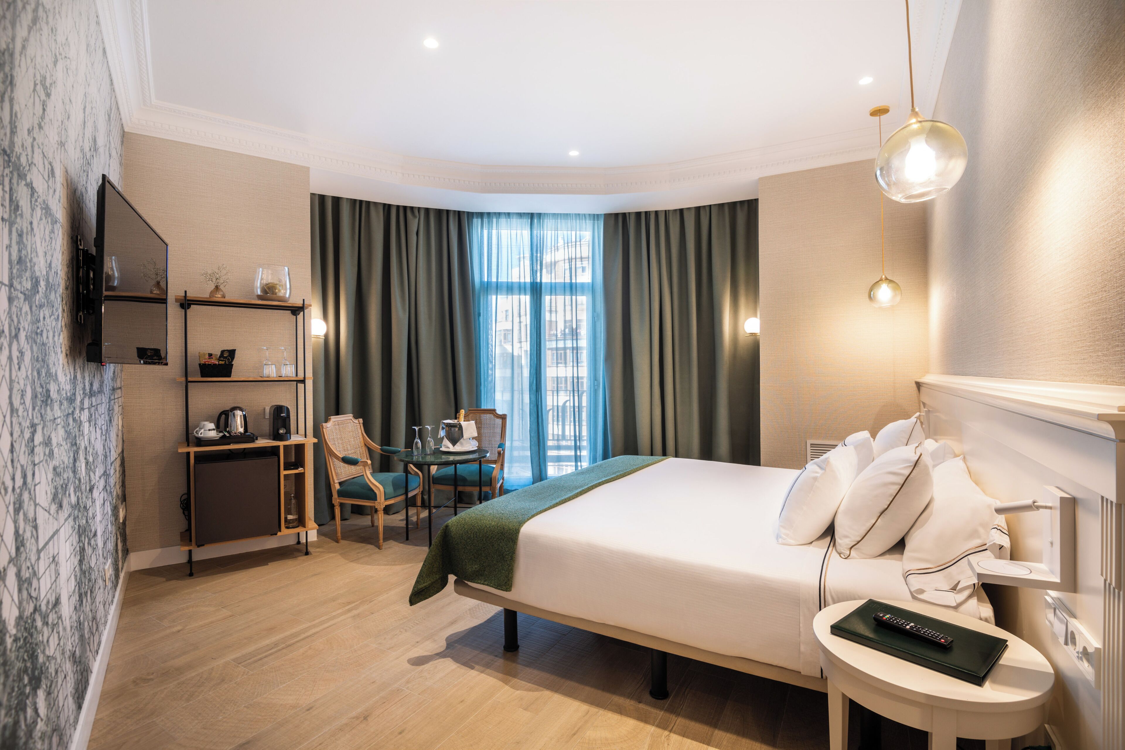 A hotel room with a bed, bedside table, desk, chair, and a TV mounted on the wall.
