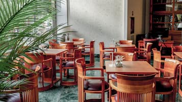 Un restaurant avec des tables et des chaises en bois, une grande plante et une bibliothèque.