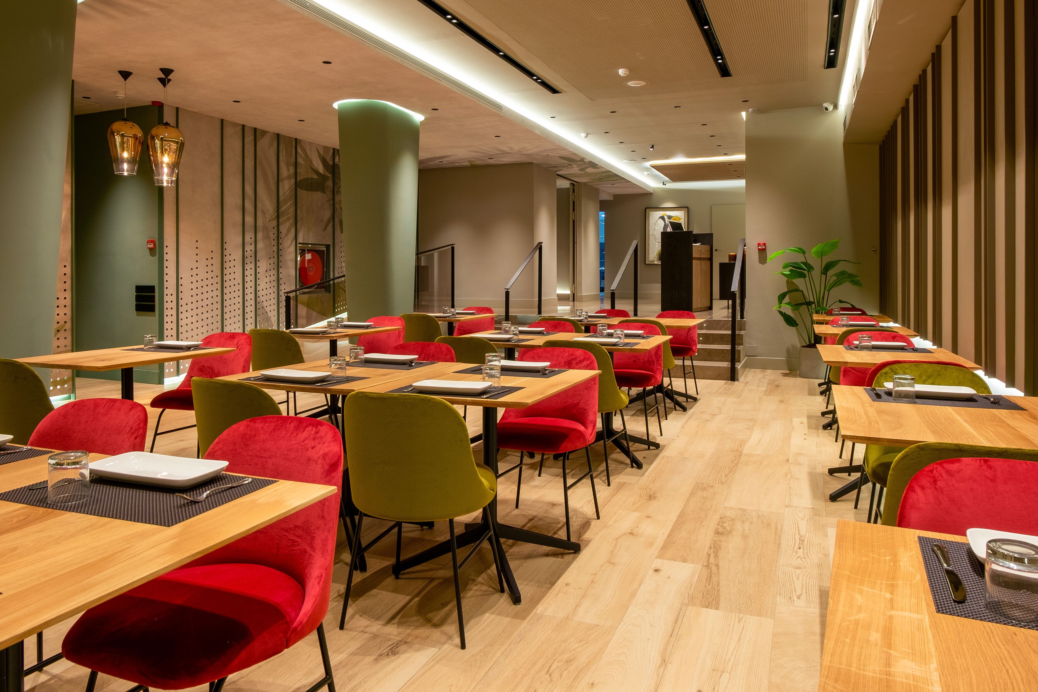A modern dining area with multiple tables and chairs, featuring a mix of red and green upholstered chairs and wooden tables.