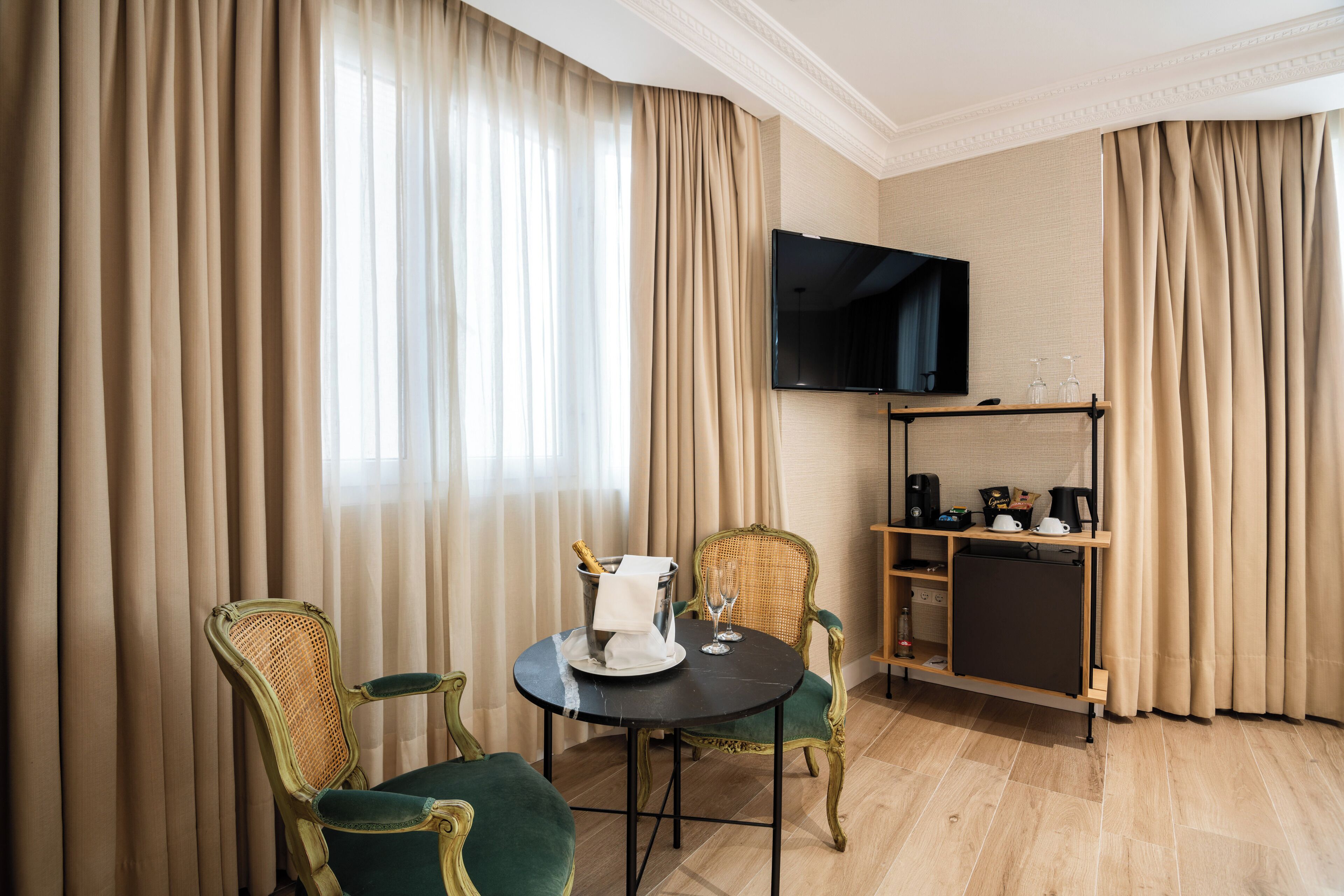 Una habitación de hotel con una mesa de comedor, dos sillas, un televisor montado en la pared y un minibar.