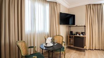 Una habitación de hotel con una mesa de comedor, dos sillas, un televisor montado en la pared y un minibar.
