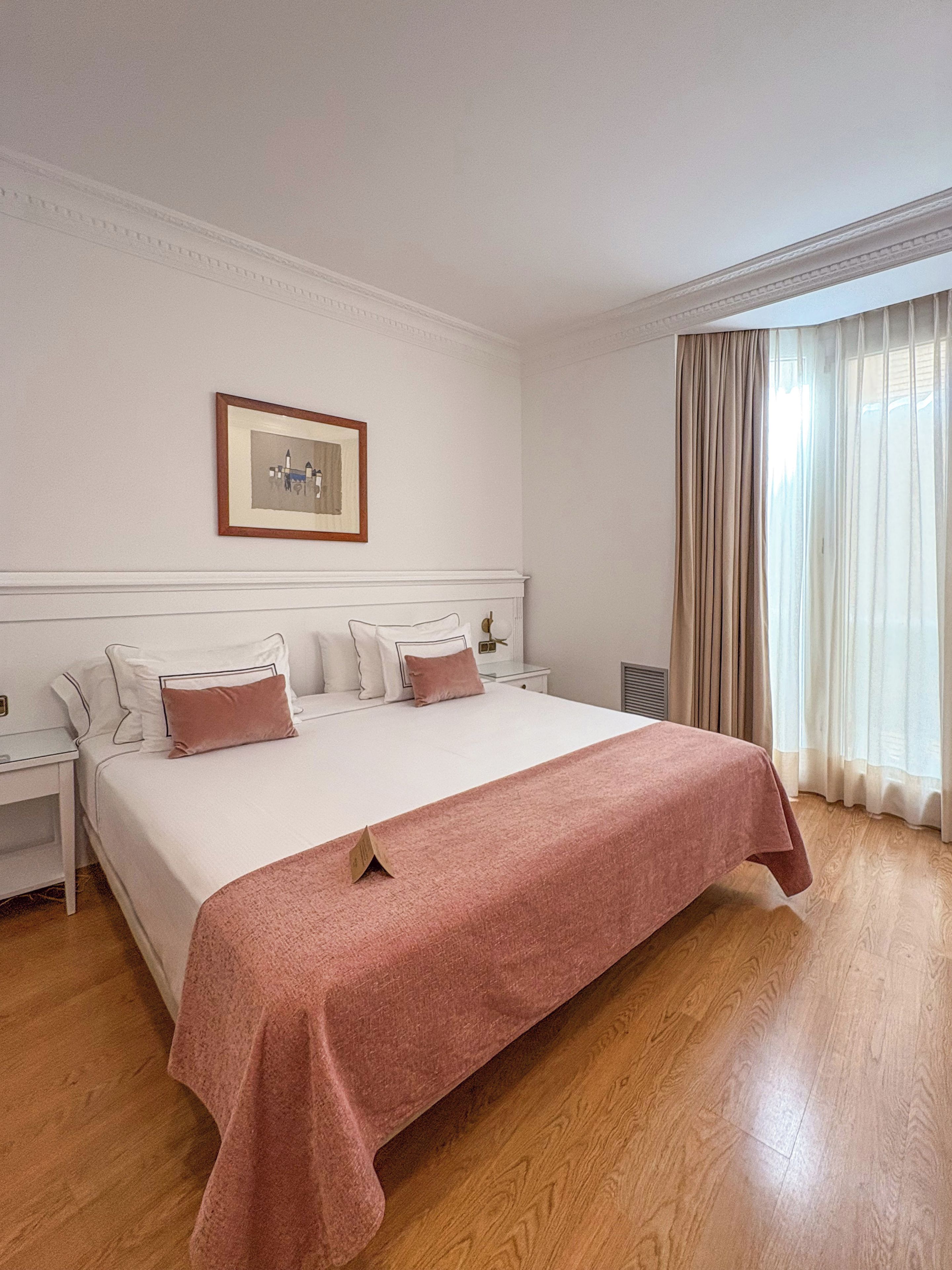 Una habitación de hotel con una cama grande, una mesita de noche y una ventana con cortinas.