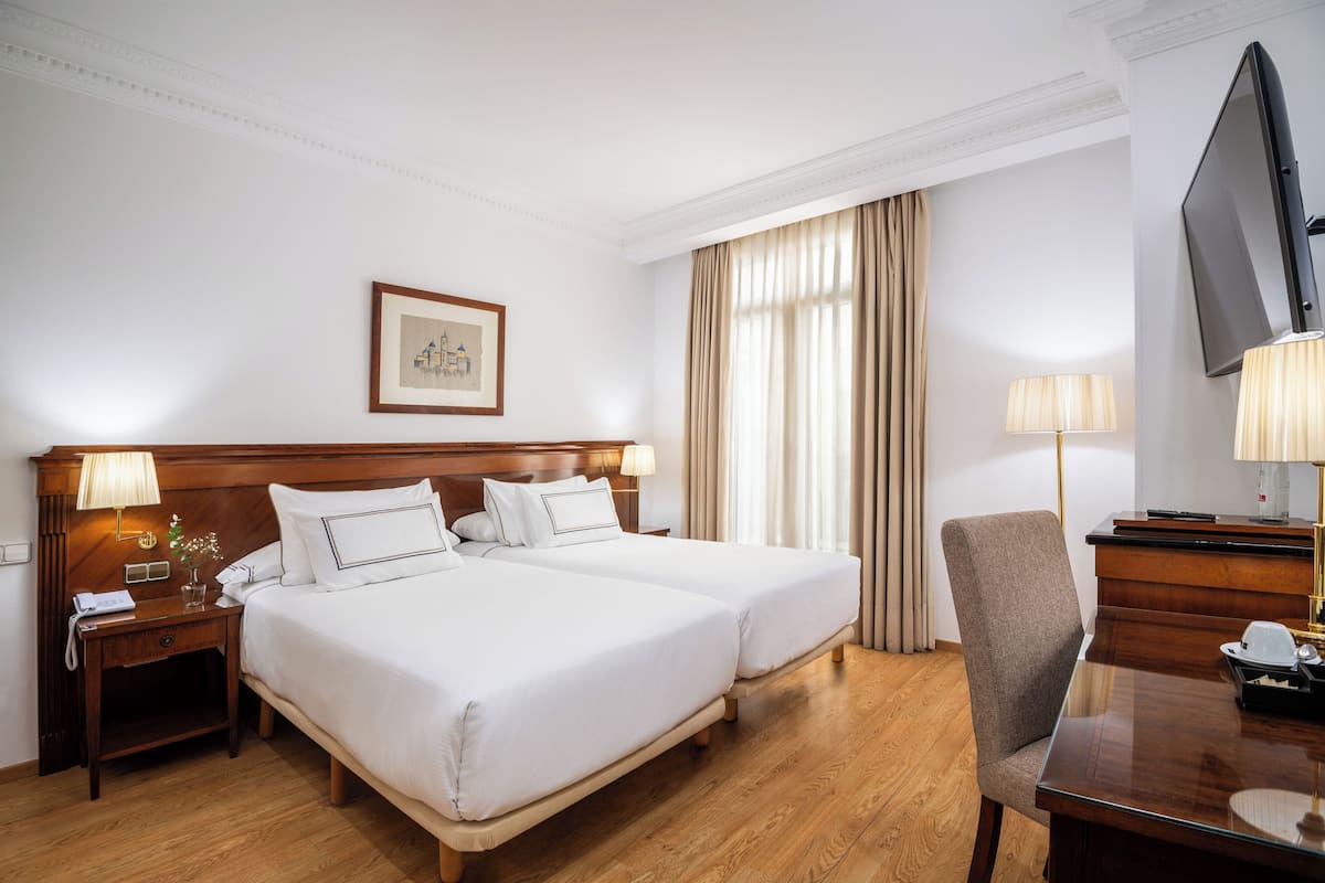 A hotel room with a double bed, a desk with a chair, a television, and a framed picture on the wall.