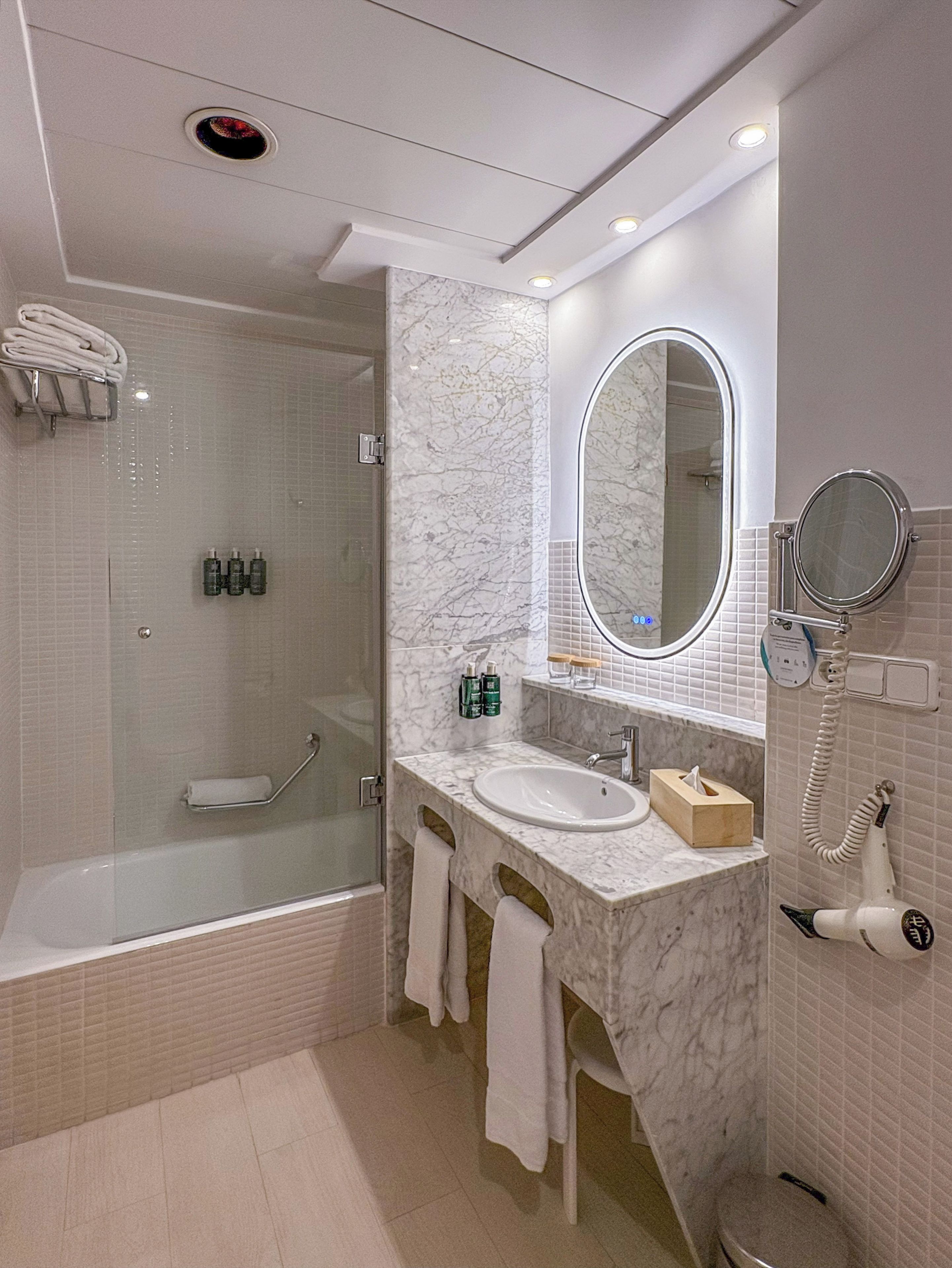 Un baño moderno con ducha envuelta en vidrio, tocador con lavamanos, espejo y secador de pelo.
