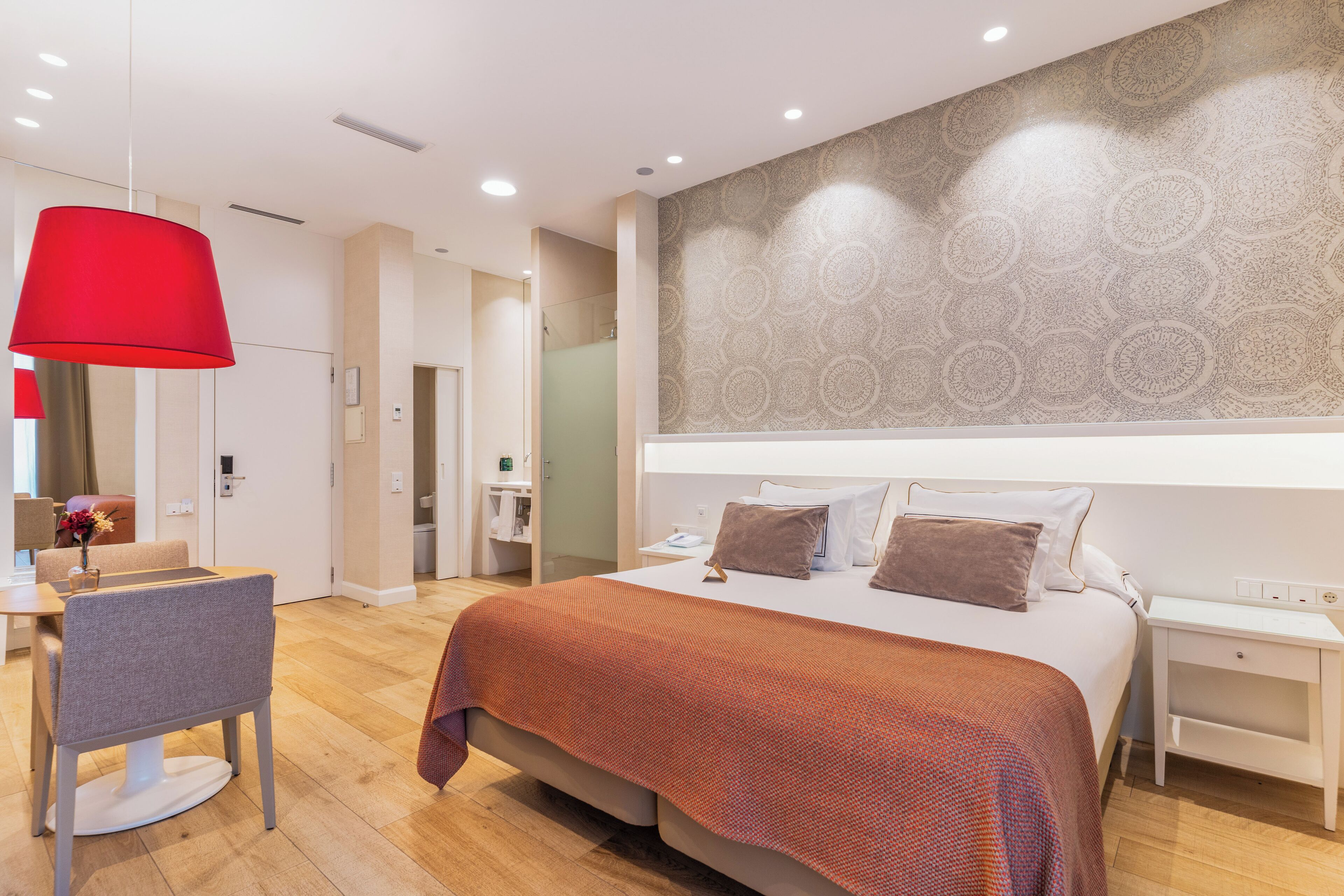 Una camera d'albergo moderna con un letto grande, una lampada pendente rossa, una parete decorata e un pavimento in legno.