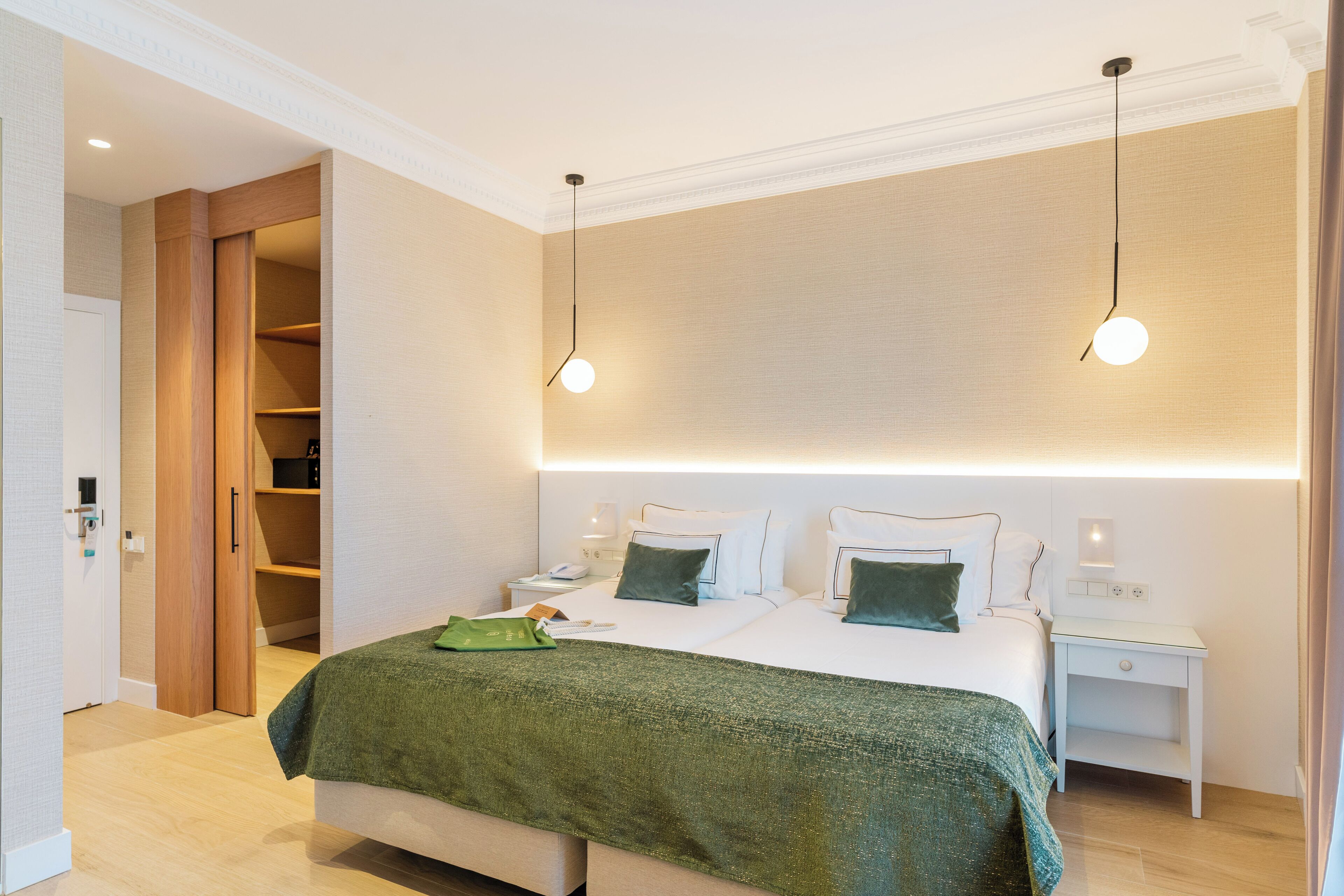 Una habitación de hotel moderna con una cama grande, mesitas de noche, un armario y una lámpara en el techo.