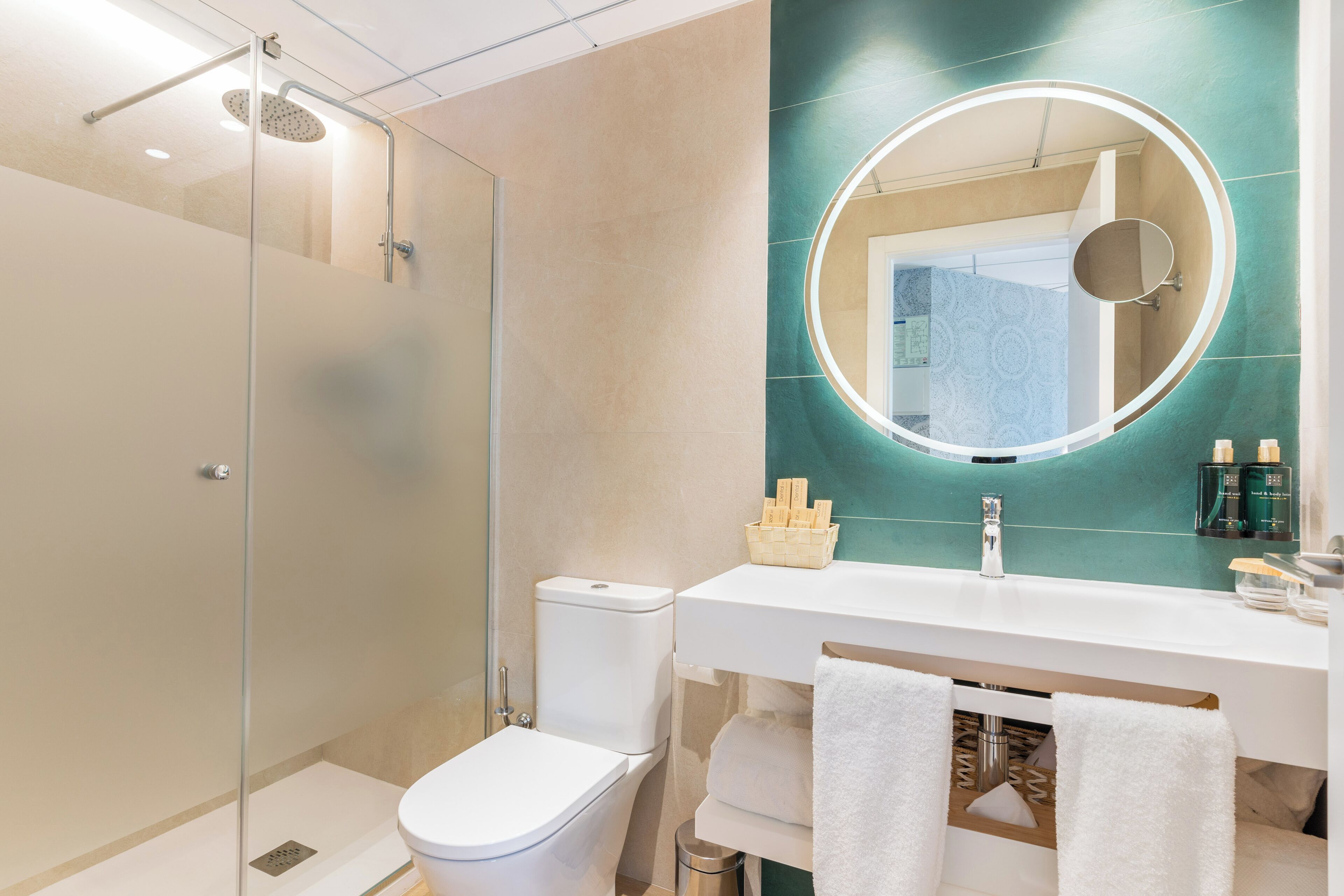 Un baño moderno con ducha envuelta en vidrio, inodoro blanco, lavamanos con espejo y toallero.