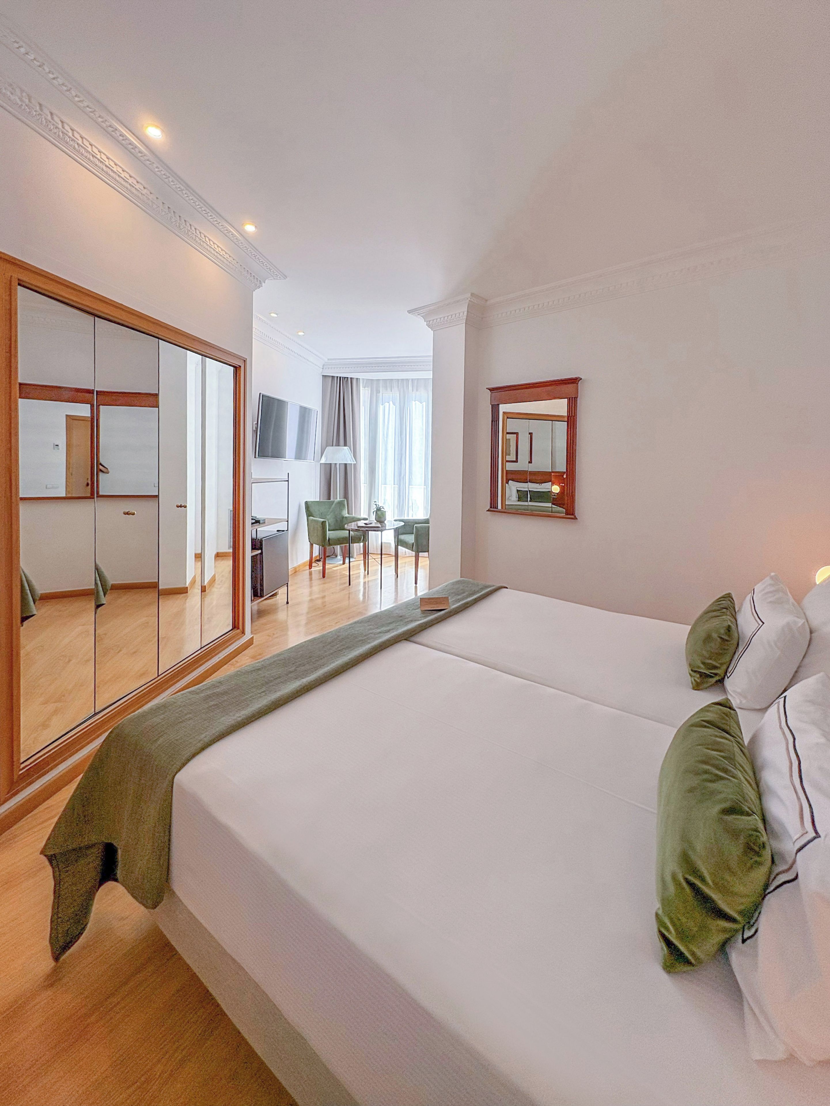 Habitación de hotel con una cama grande, un espejo, un televisor y una zona de estar con una mesa y sillas.