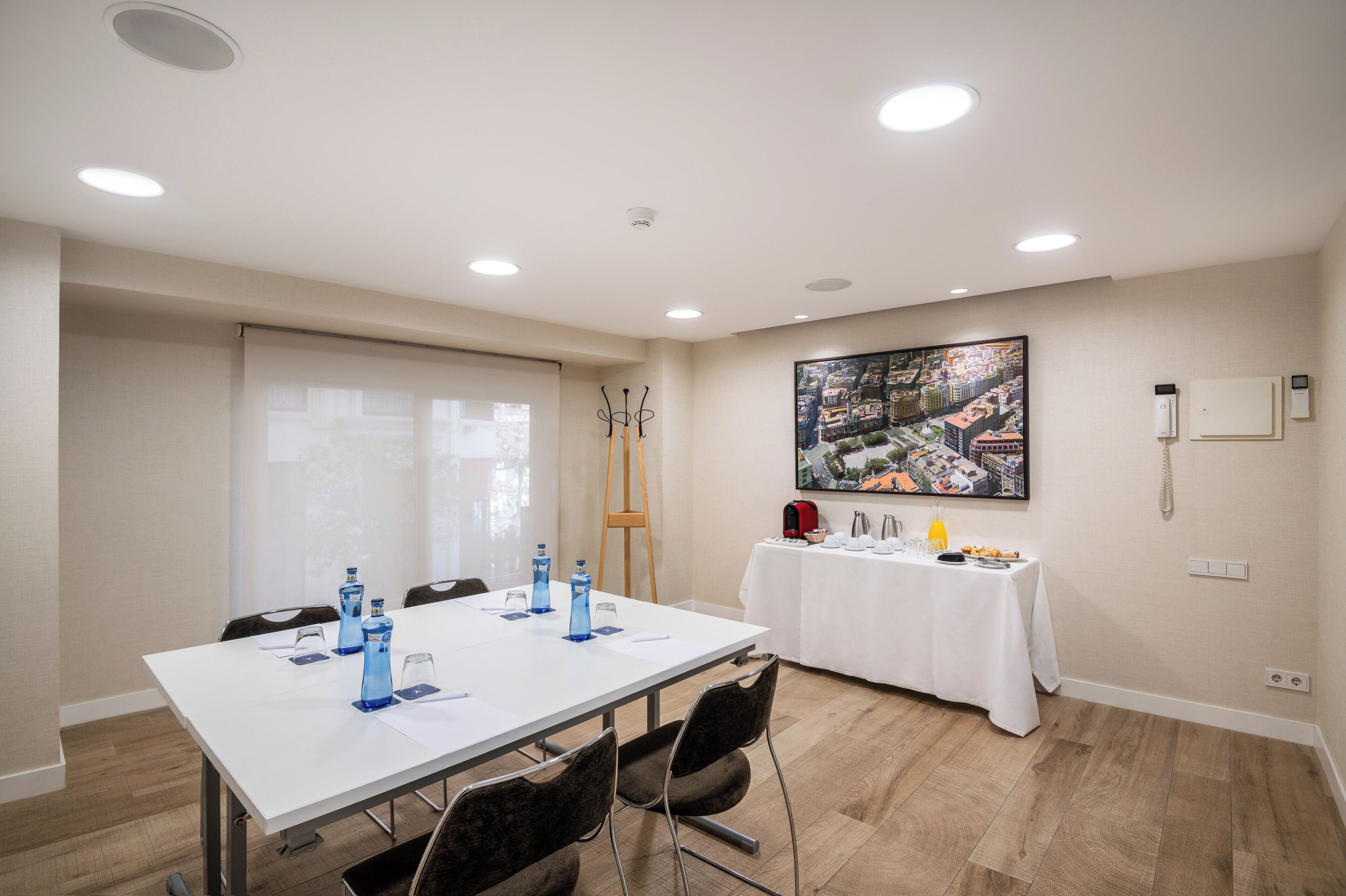 A conference room with a white table, chairs, and a white tablecloth. There are water bottles, a projector, and a painting on the wall.