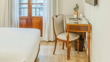 Een hotelkamer met een bed, een houten bureau met stoel, een televisie en een raam met gordijnen.