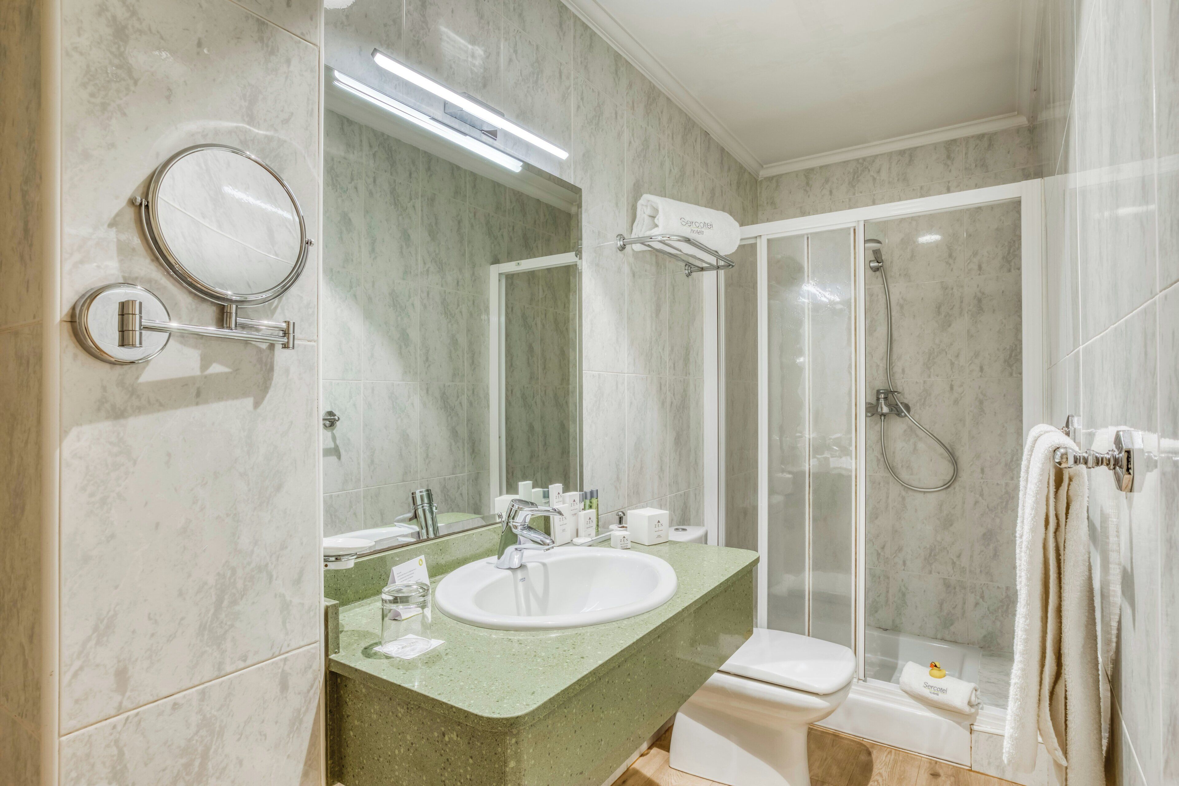 Un baño con pared de mármol, un lavabo con espejo, un inodoro y una zona de ducha.