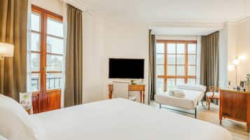 Habitación de hotel con una cama grande, un escritorio con televisor de pantalla plana, una silla y vistas de la ciudad a través de amplias ventanas.
