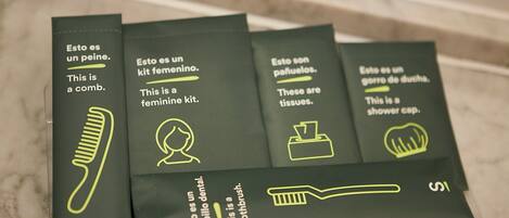 Fire grønne bokse med tekst og ikoner, hver mærket med en anden ting: kam, toilettaske til kvinder, lommetørklæder og brusehuet.
