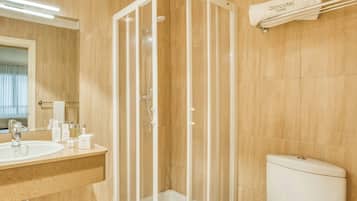 Un baño con ducha de vidrio, lavamanos con artículos de aseo y retrete.