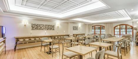 A spacious dining area with multiple tables and chairs, a wooden floor, and a high ceiling with skylights.