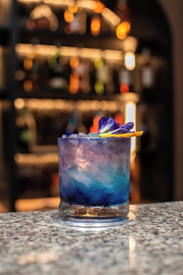 A bar setting with a glass of blue cocktail garnished with a flower and an orange slice.