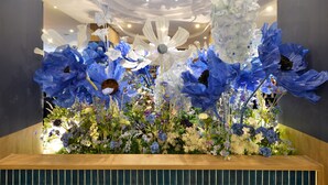 Uma exposição floral com flores grandes em azul e branco em um ambiente interno moderno.