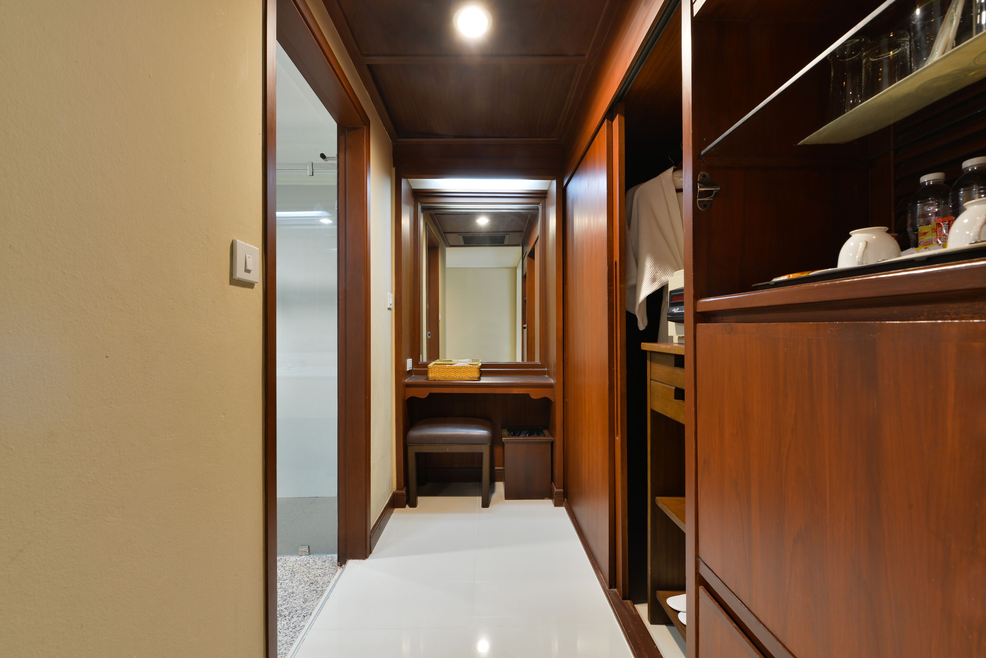 A narrow hallway with a wooden bench, a small trash bin, and a shelf with kitchenware.