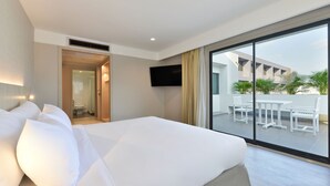 Quarto de hotel com cama grande, televisão fixada na parede e varanda com mobiliário exterior.