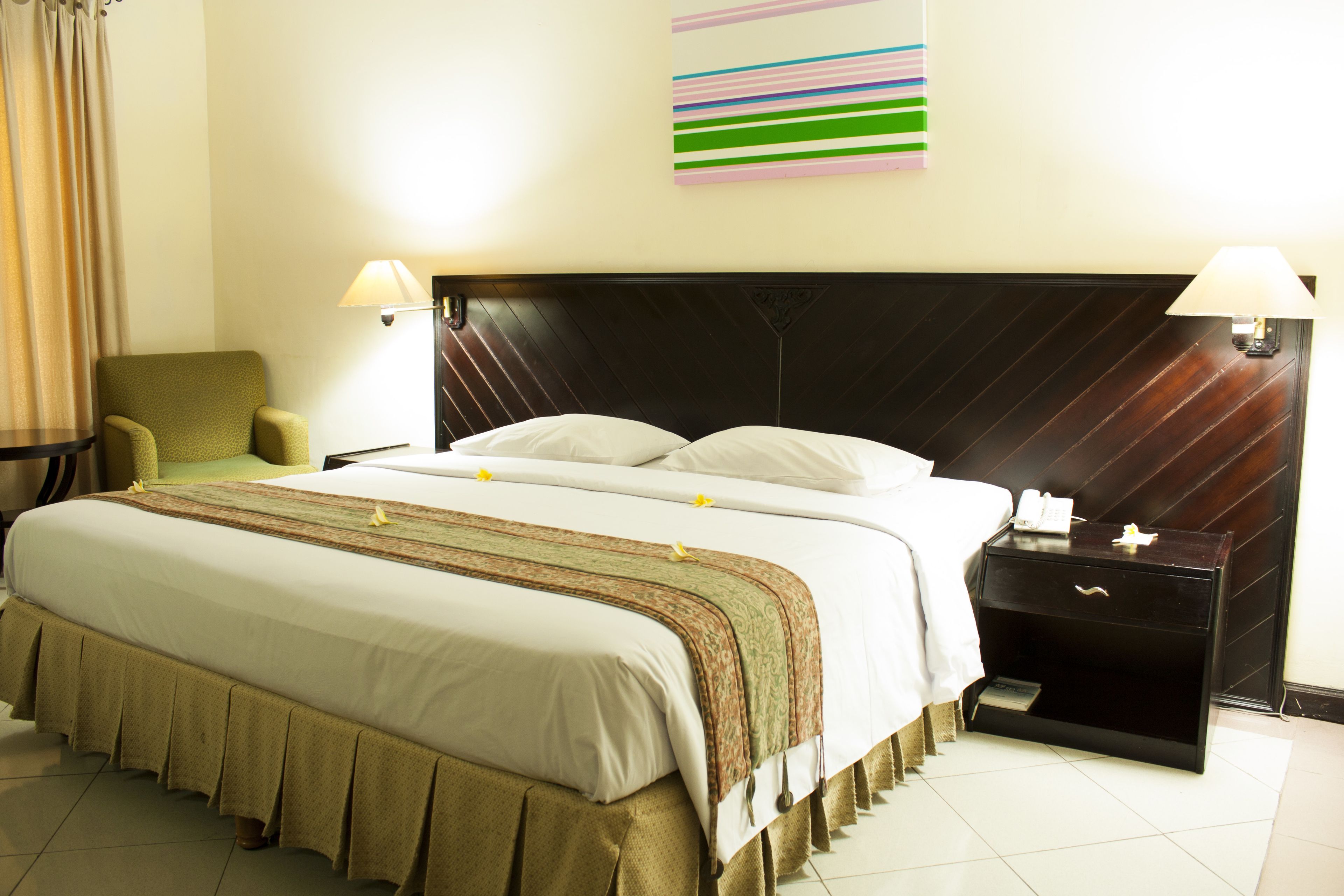 Une chambre d’hôtel avec un grand lit, une table de chevet avec une lampe, une chaise et un élément décoratif mural.