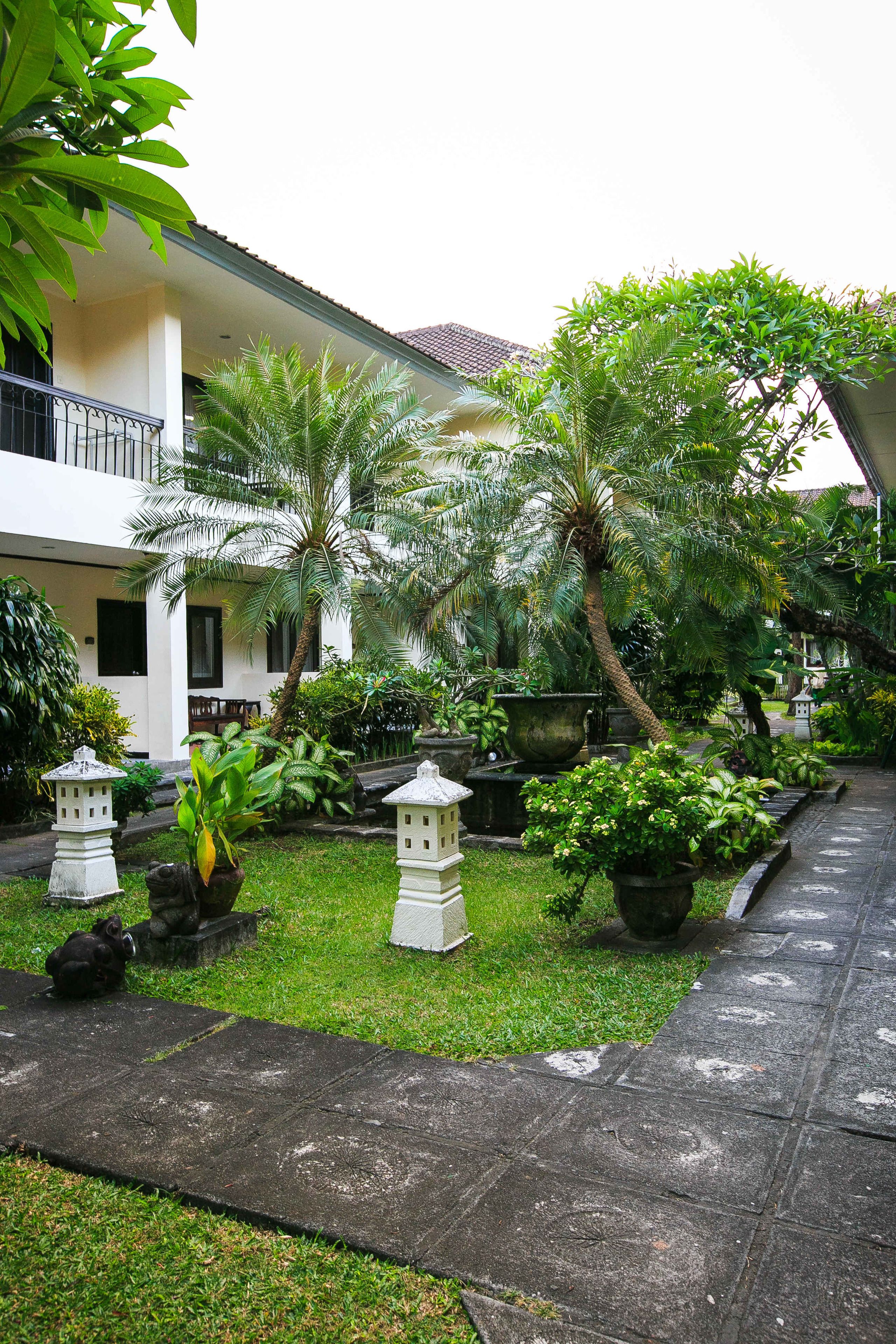 A courtyard with a pathway, potted plants, and a building with a balcony.