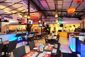 A restaurant with multiple dining tables and chairs, a bar area, and a stage for live performances. - Legian Paradiso Hotel (Legian)