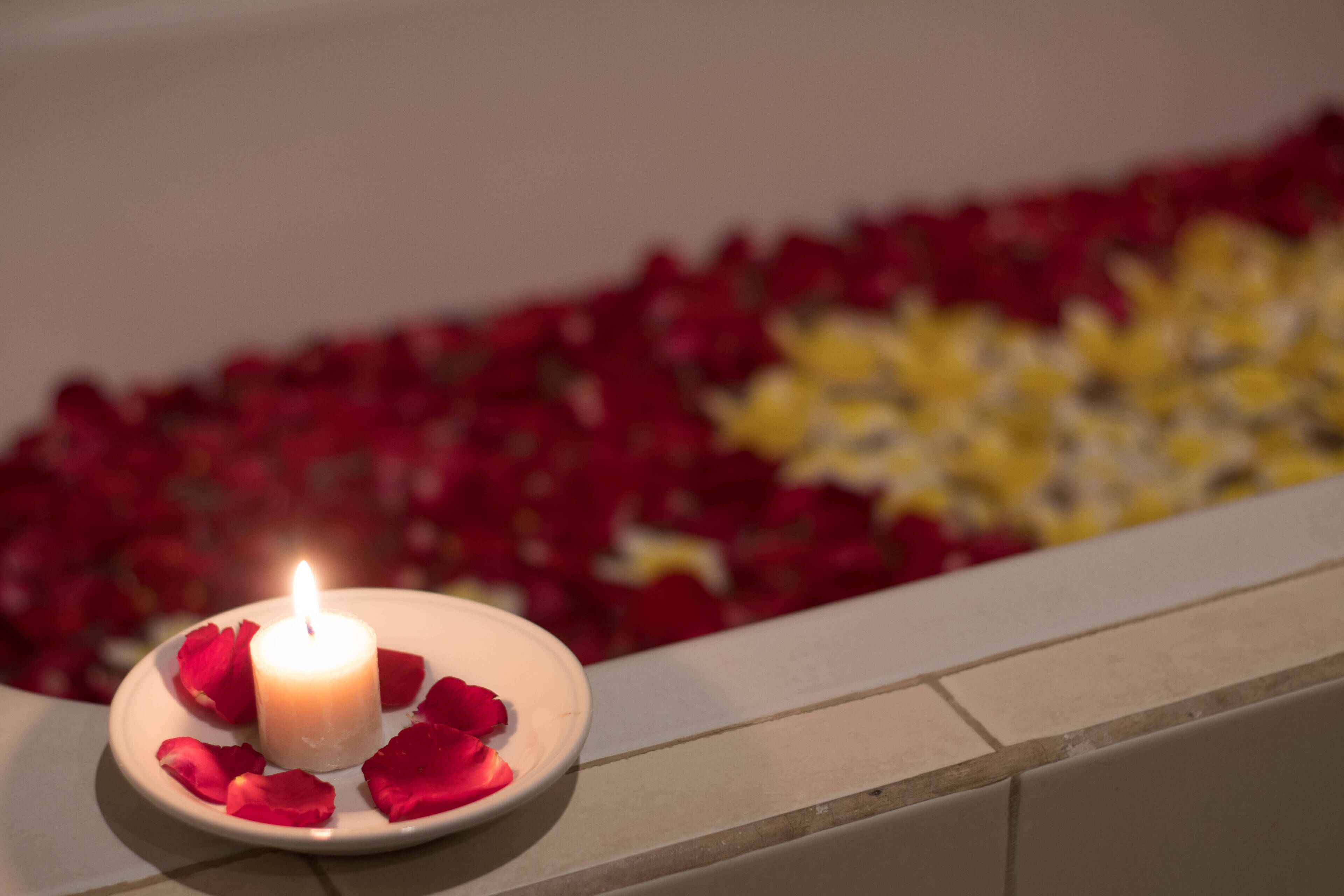 A lit candle on a plate with rose petals, surrounded by a bed of red and yellow flowers.