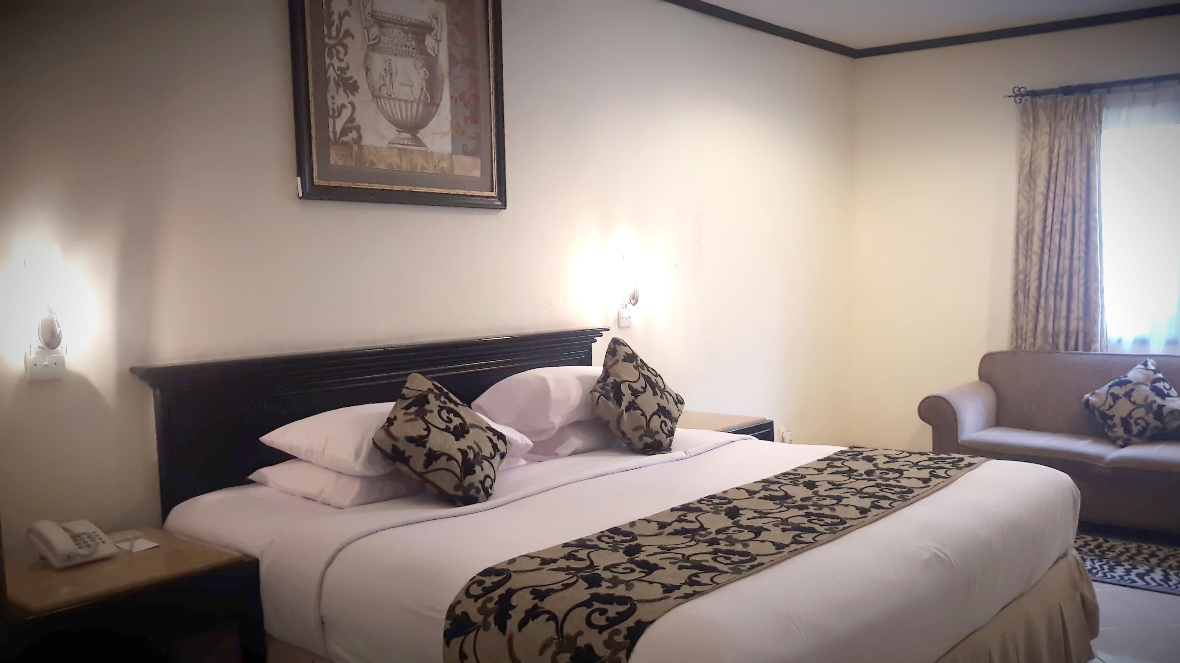 A hotel room with a large bed, a nightstand with a phone, a sofa, and a framed picture on the wall.