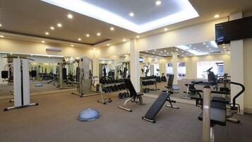 Un gimnasio con diversos equipos de ejercicio, espejos e iluminación empotrada en el techo.