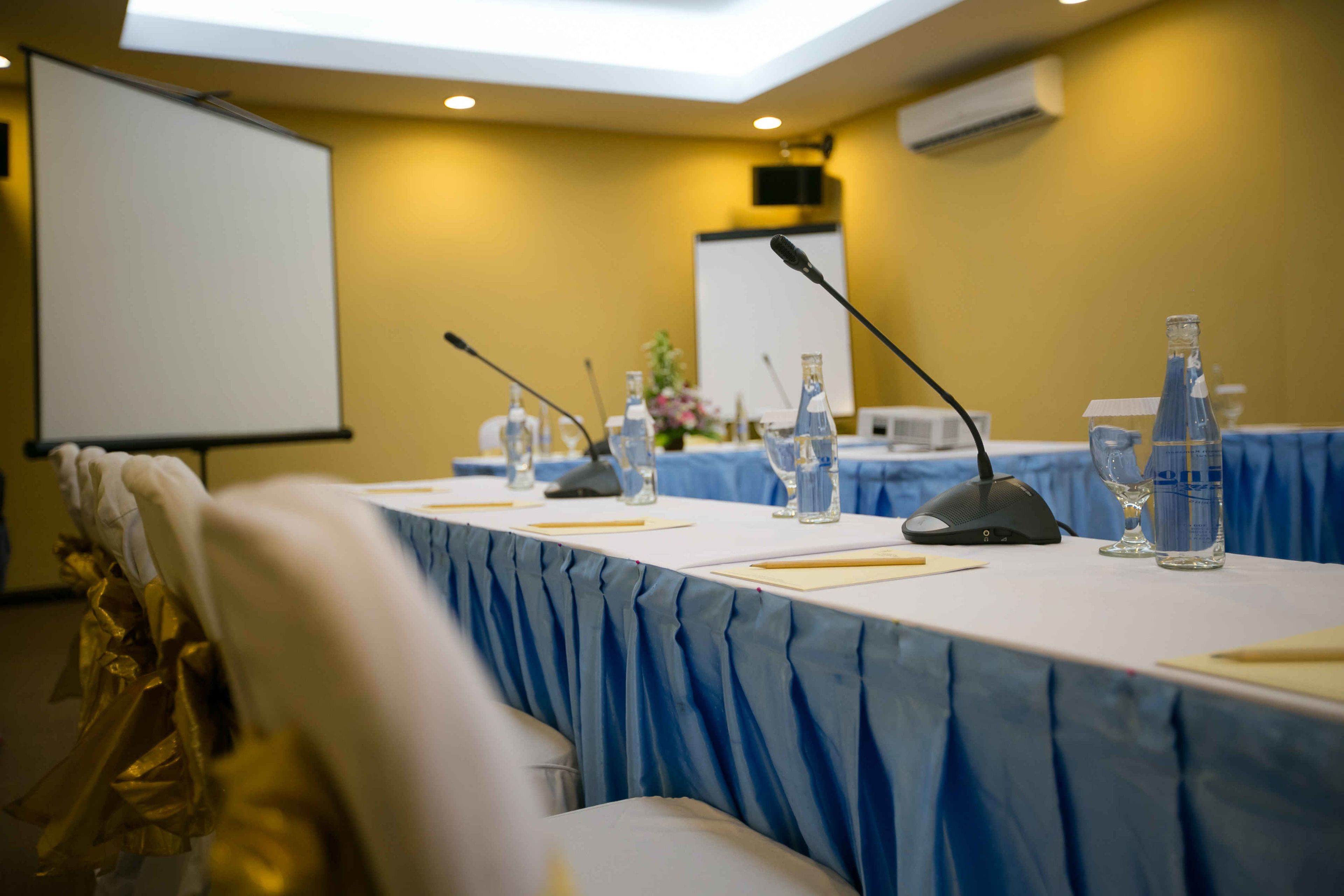 A conference room with a long table, microphones, water bottles, and a whiteboard.