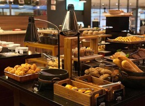 Un buffet proposant une variété de produits de boulangerie, notamment des pâtisseries et du pain, présentés sur des présentoirs et des plateaux en bois.