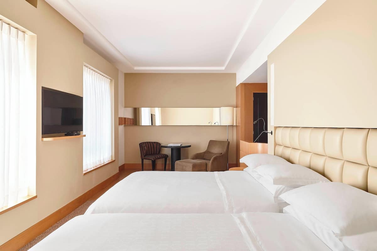 A hotel room with two beds, a TV, a desk, and a chair.
