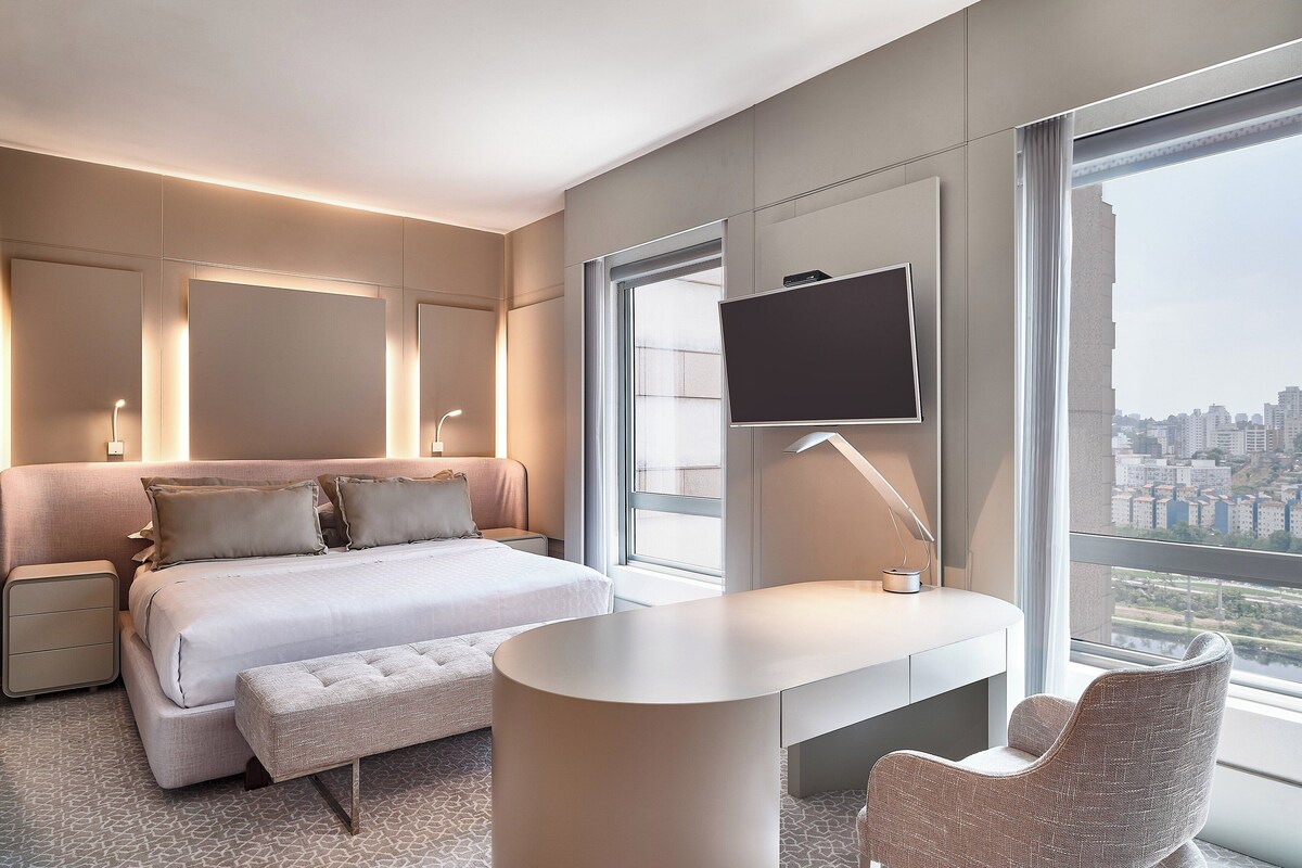 Une chambre d’hôtel moderne, dotée d’un grand lit, d’un bureau, d’une chaise et d’un téléviseur fixé au mur.