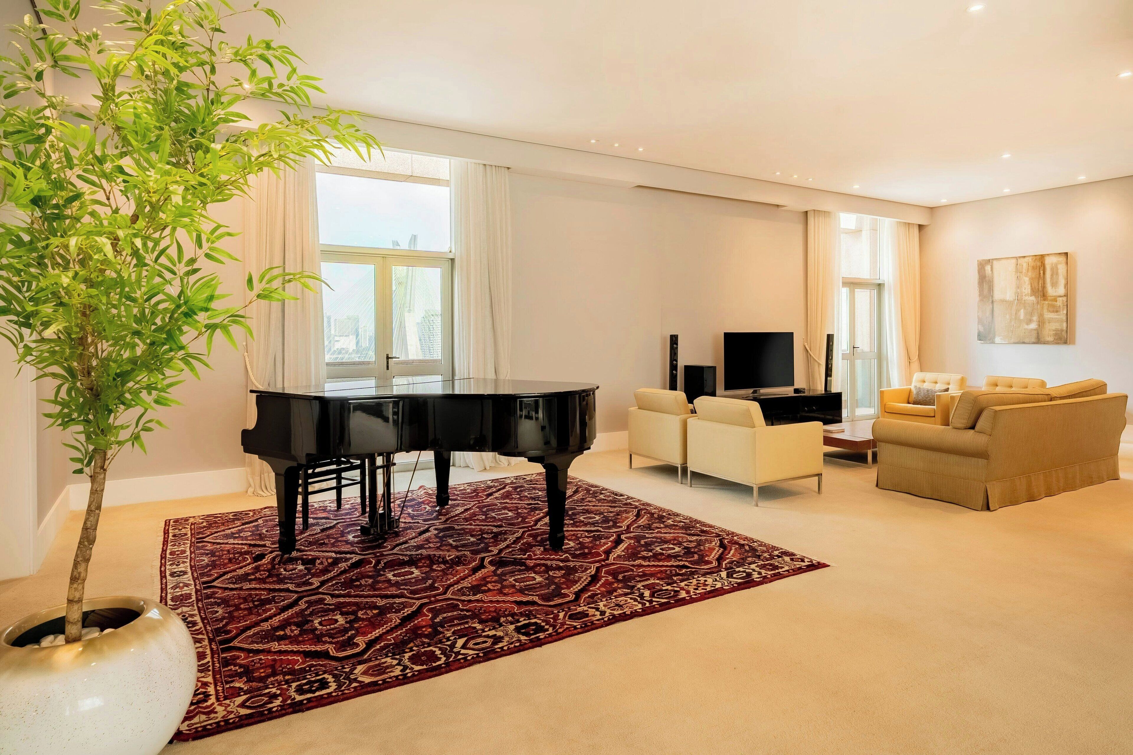 A living room with a grand piano, a beige sofa, a coffee table, and a large window with curtains.